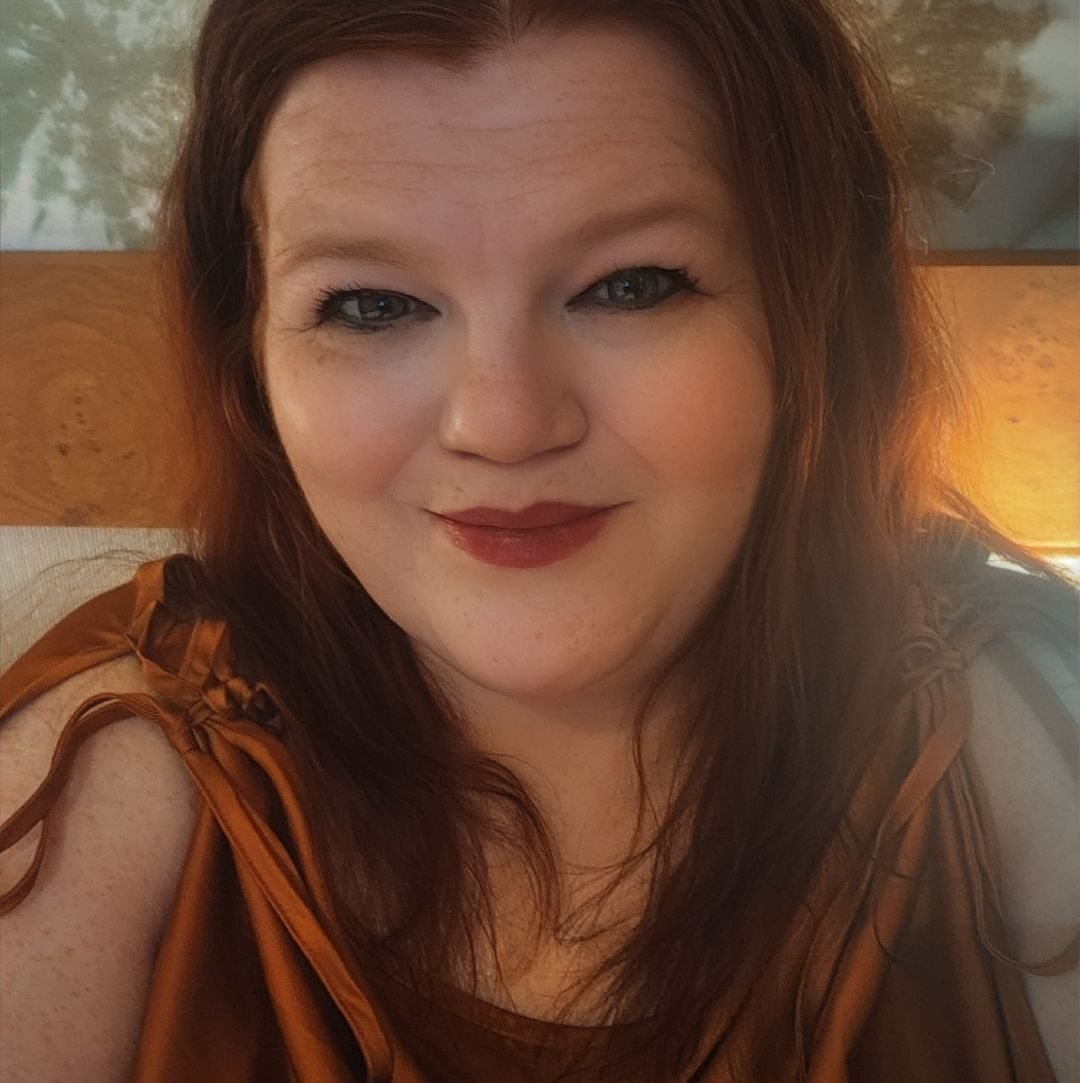 Photo of D Kai Wilson-Viola, Japan, 2025. Redheaded woman in makeup with blue eyes, smiling